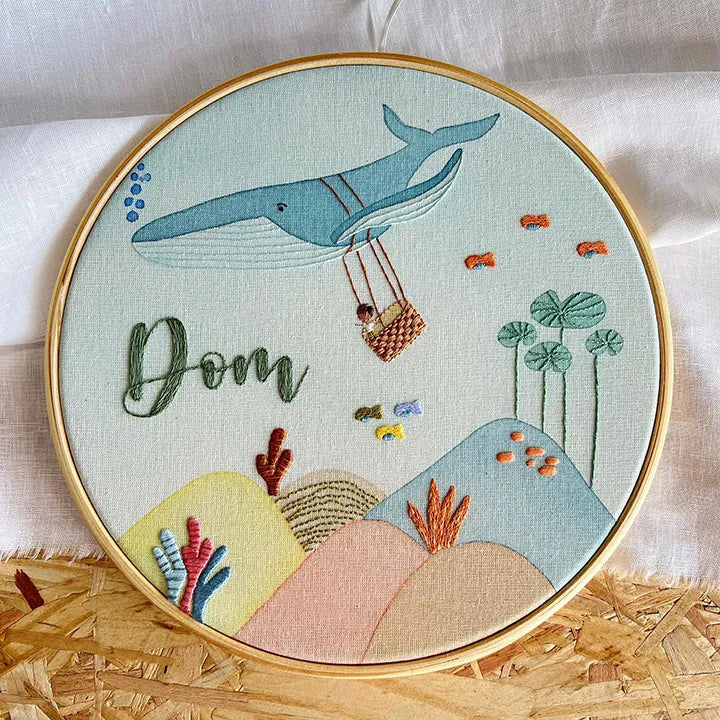 Embroidery hoop with whale and child design, featuring the name 'Dom'.