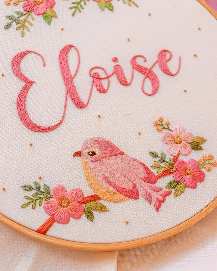Close-up view of floral clock embroidery with pink petals and bird stitching