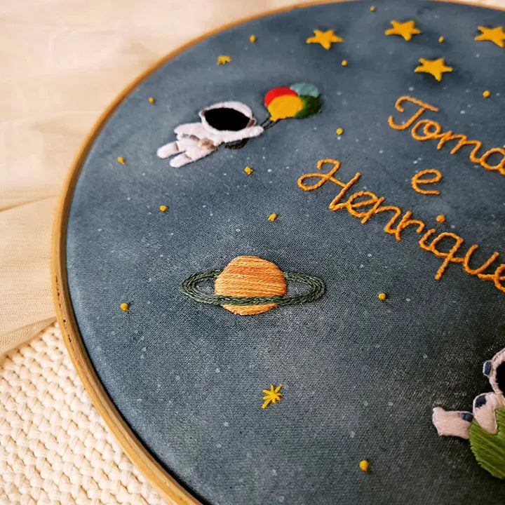 Custom Embroidery hoop with space-themed design including an astronaut, planet, and stars on a dark blue fabric.