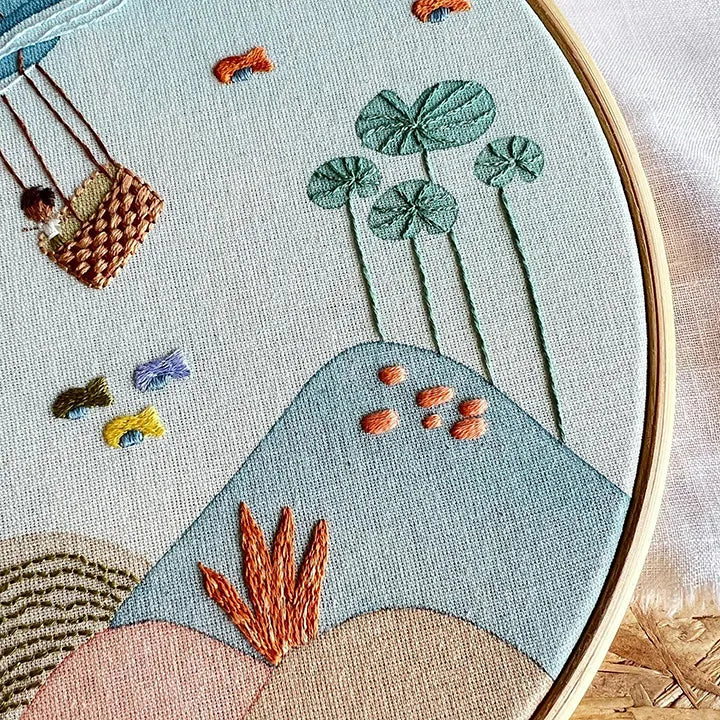 Embroidery hoop with a scenic design featuring plants and a swing.