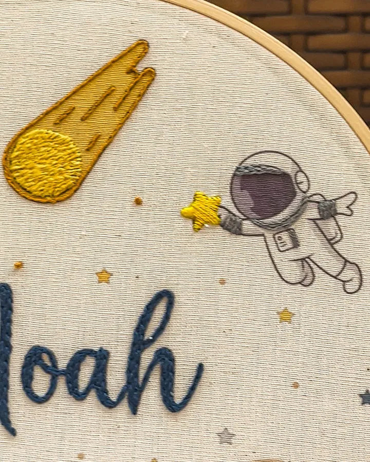 Embroidery hoop with embroidered design of an astronaut, comet, and stars
