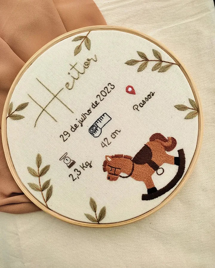 Embroidery hoop with embroidered details of a baby's birth information and a horse design.