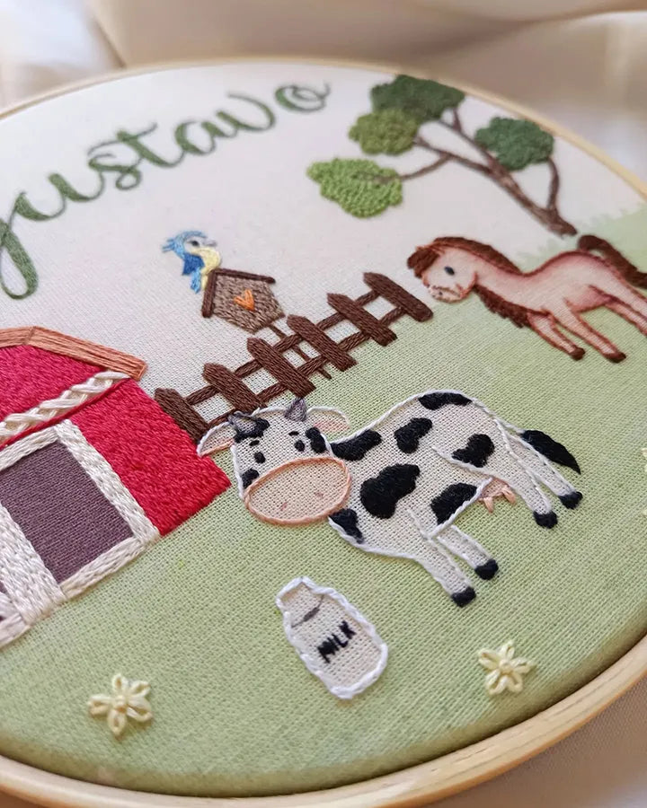 Embroidery hoop with farm-themed design including a cow, barn, and horse.