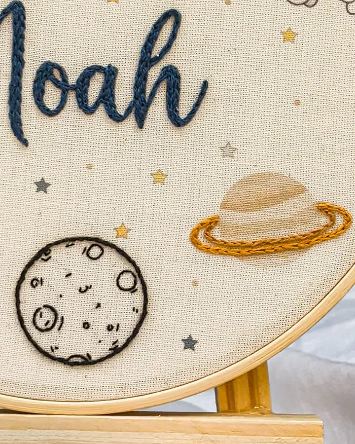 Embroidery hoop with name embroidered, moon, and space-themed design.