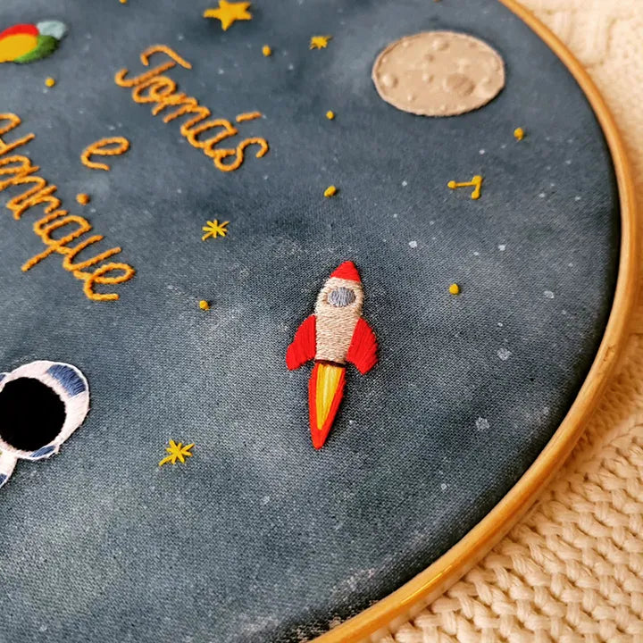 Embroidery hoop with space-themed design including a rocket, stars, and moon.