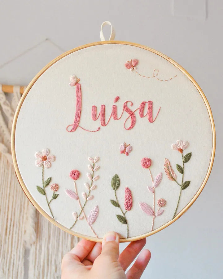 Embroidery hoop with name embroidered, surrounded by floral patterns.