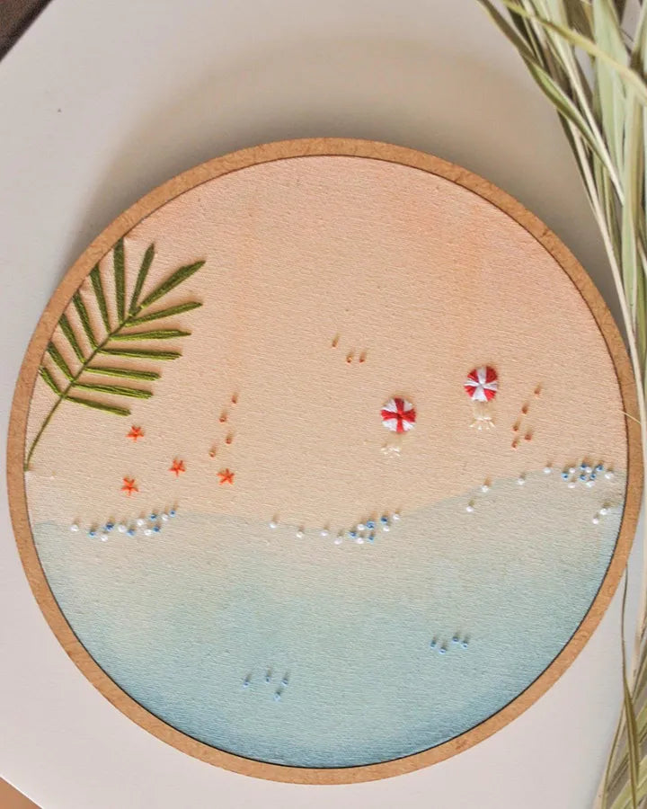 Embroidery hoop with a beach scene design featuring palm leaves and umbrellas.